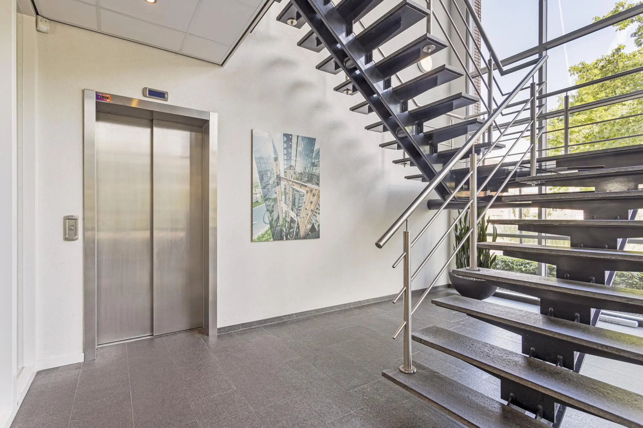 Moderne trappenhal met metalen trap, lift en een afbeelding van de Fascinatio Boulevard aan de muur.